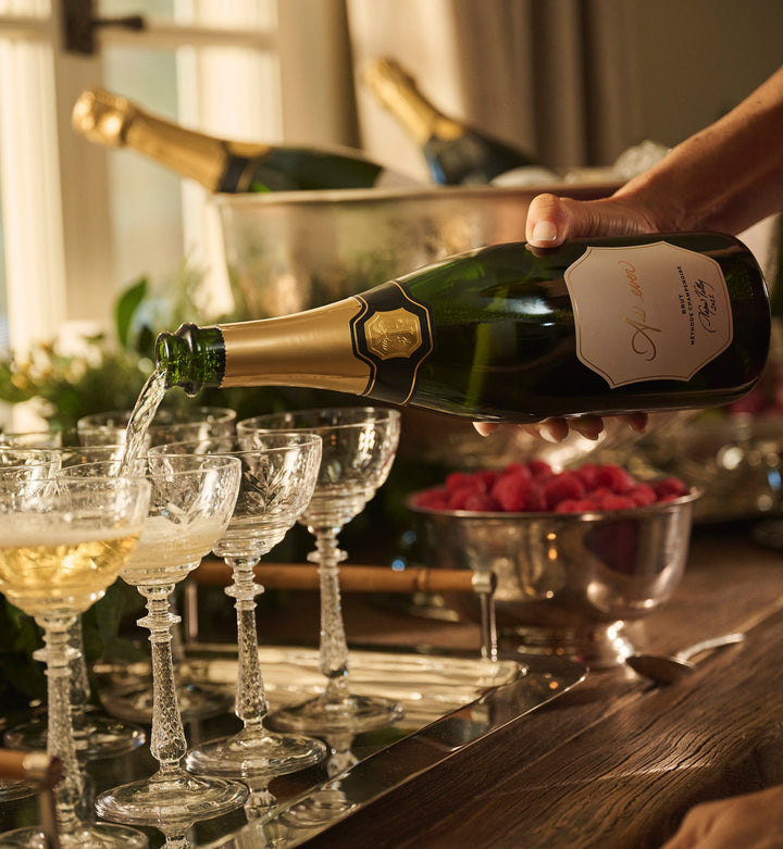 Meghan pouring As ever Brut into wine glasses on a silver platter beside berries, greenery, and bottles of wine